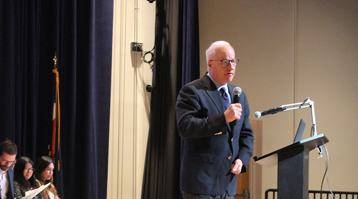 Mayor Mike, a man with white hair, giving a speech at a podium with a microphone.